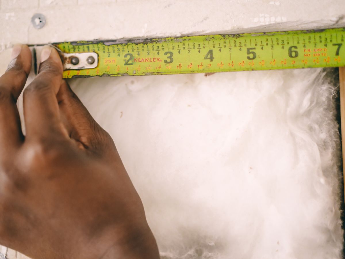 A hand measuring insulation with a tape measure